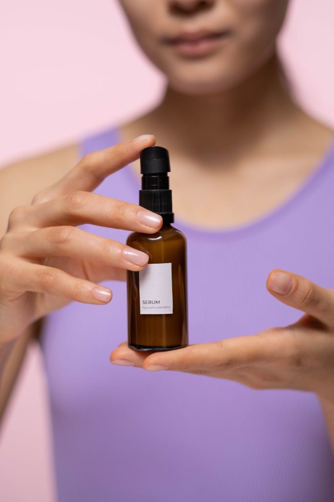 Woman holding a skincare serum bottle against a pink background